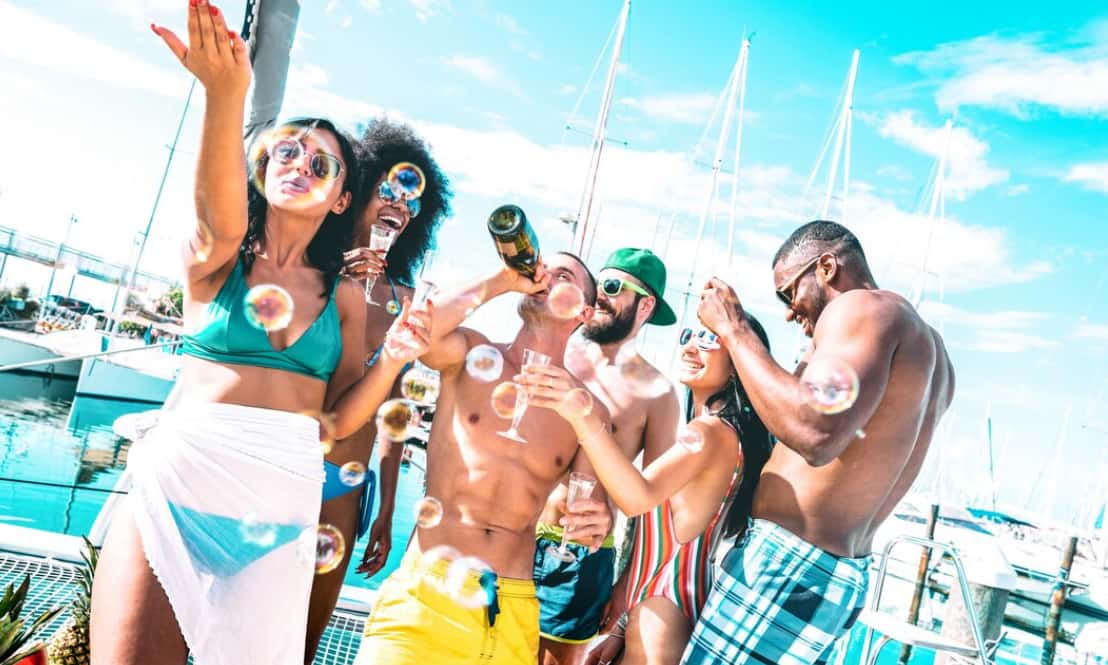 people partying with drinks by yachts, bubbles floating around
