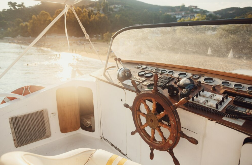 A weathered boat helm with a view of a sunlit beach