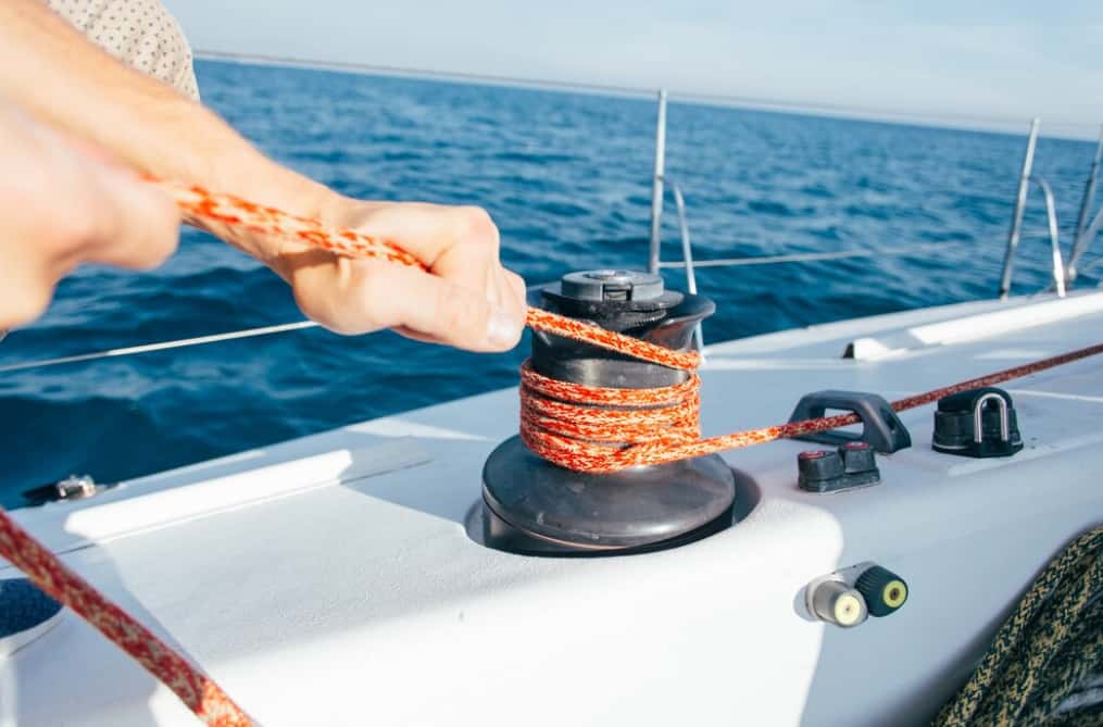 A person coiling an orange rope on a boat's winch