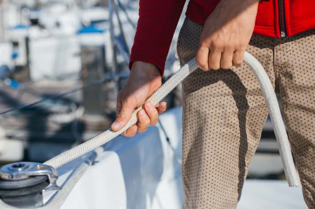 Close-up of hands coiling a white rope on a yacht's side